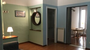 Un salon comprenant un canapé, une lampe, un tableau encadré, un miroir et une porte donnant sur un coin repas.