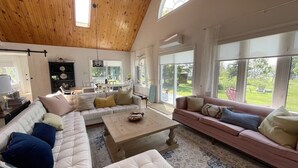 Amplia sala de estar con techo de madera alto, ventanas grandes y una zona de estar acogedora con sofá y sillón.