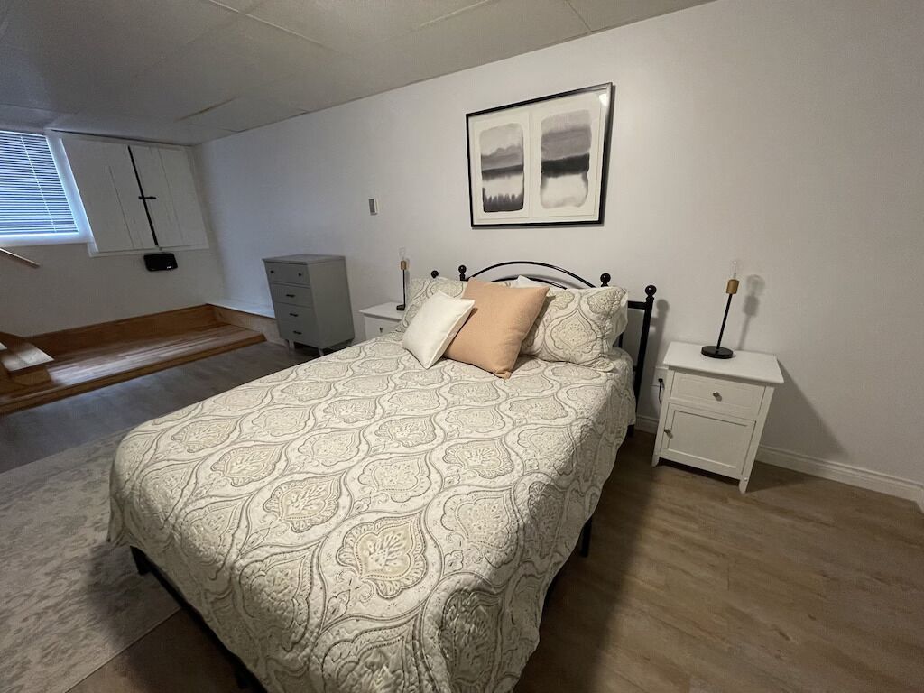 Quarto com cama, mesas de cabeceira, cômoda e janela com persianas.