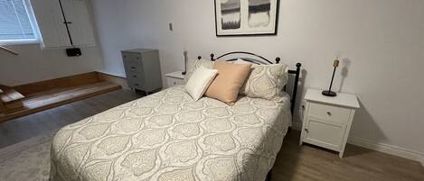 Quarto com cama, mesas de cabeceira, cômoda e janela com persianas.