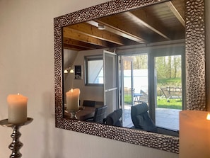 Un miroir doté d’un cadre texturé qui reflète une pièce comprenant un lit, une table et une vue sur un patio aménagé avec du mobilier d’extérieur.