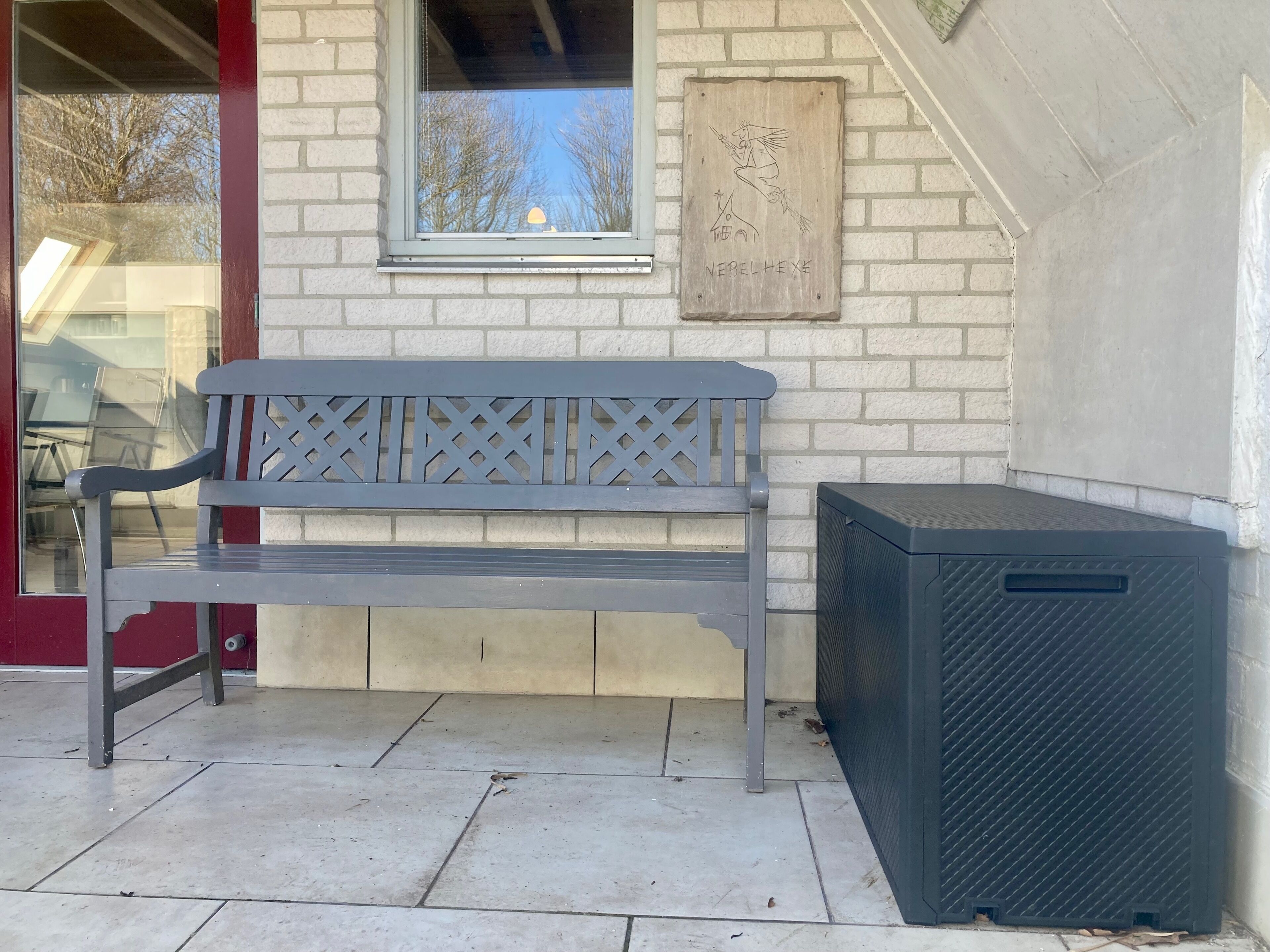 A bench, a trash bin, and a window with a view of trees.