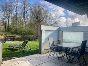 A patio with a table and chairs, a swing, and a view of a pond and trees.