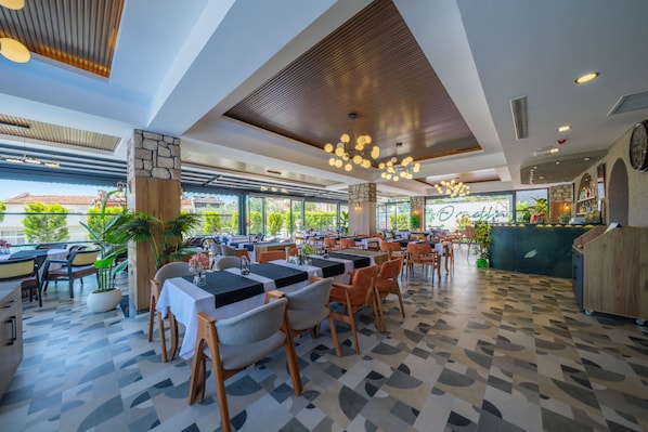 Un restaurante moderno con un patrón geométrico en el suelo, mesas y sillas de madera, y vistas al exterior con vegetación.