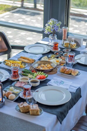 Une table dressée avec différents plats, notamment du pain, des légumes et un bol de nourriture, avec une vue sur une fenêtre en arrière-plan.