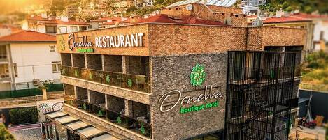 A hotel with a restaurant on the ground floor, a pool area, and a view of a hillside town.