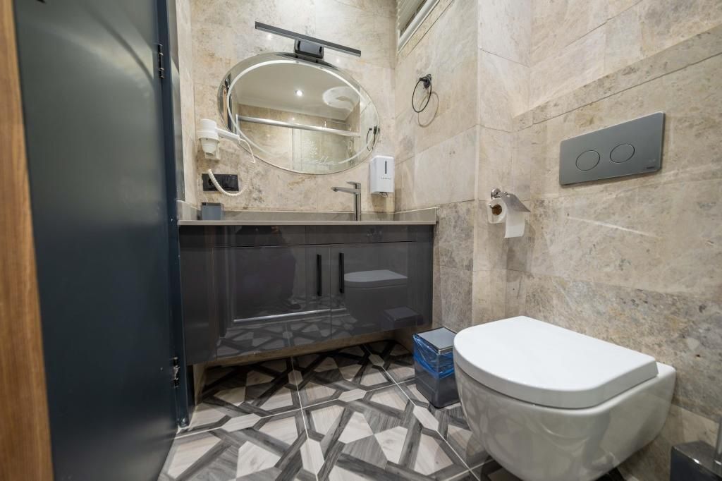 A modern bathroom with a glass-enclosed vanity, a white toilet, and a marble-tiled floor.