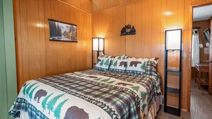 Un dormitorio con cama, paredes de madera, un cuadro y una mesita de noche.