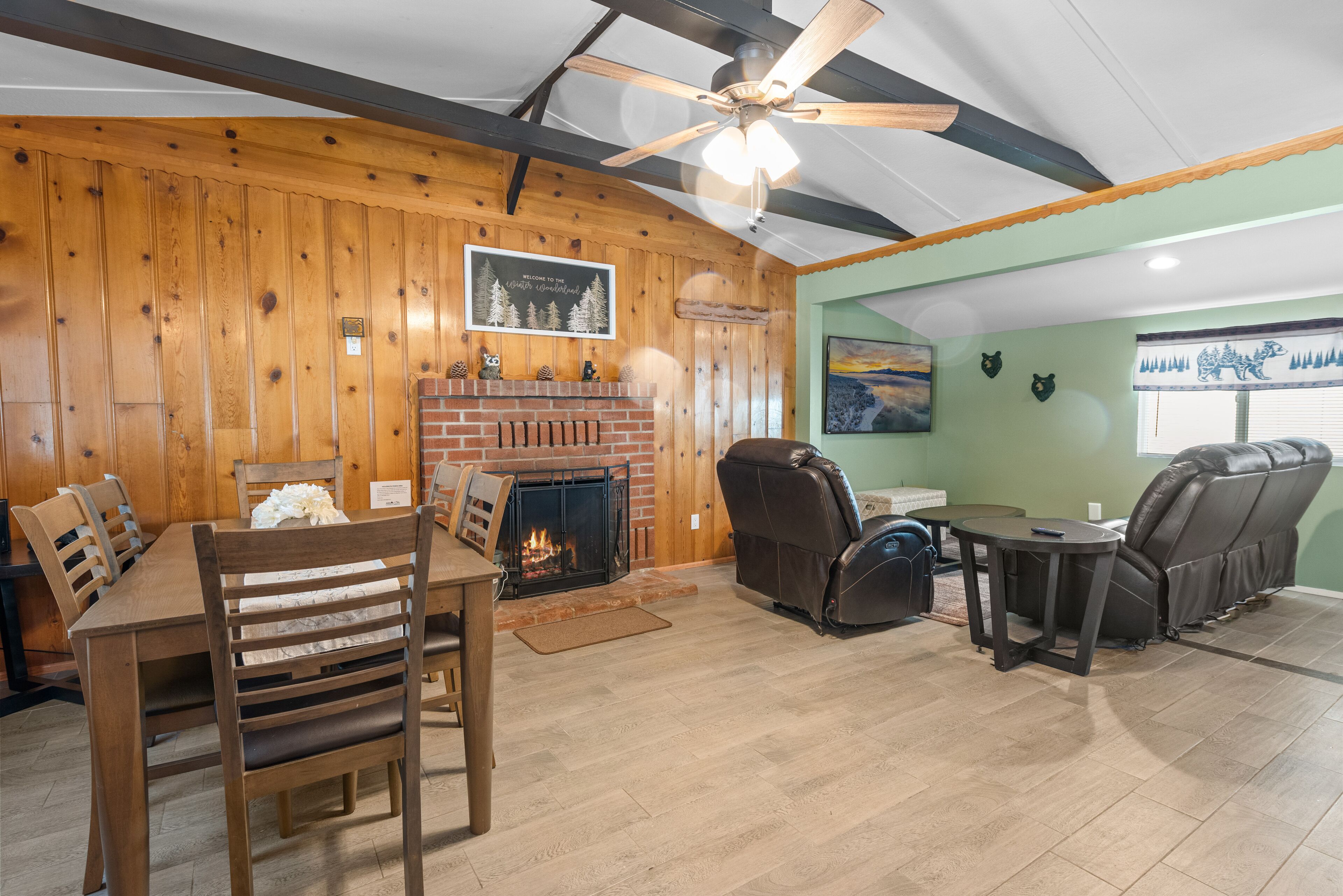 A cozy living room with a fireplace, wooden walls, and a ceiling fan.