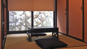 A traditional Japanese room with tatami flooring, a low table with cushions, and a view of a rocky garden through large windows. - Kiyomizu Birodo-An (Kyoto)