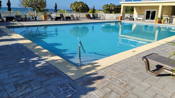 A swimming pool with a clear view of the ocean, surrounded by lounge chairs and potted plants. - Draxhall Marina Villa (St. Ann's Bay)