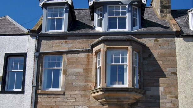 Un coin d’un bâtiment avec une façade en pierre, une baie vitrée et une lucarne.