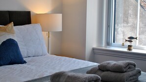 Una cama bien hecha con almohadas blancas y azules, una lámpara y toallas dobladas en un alféizar.
