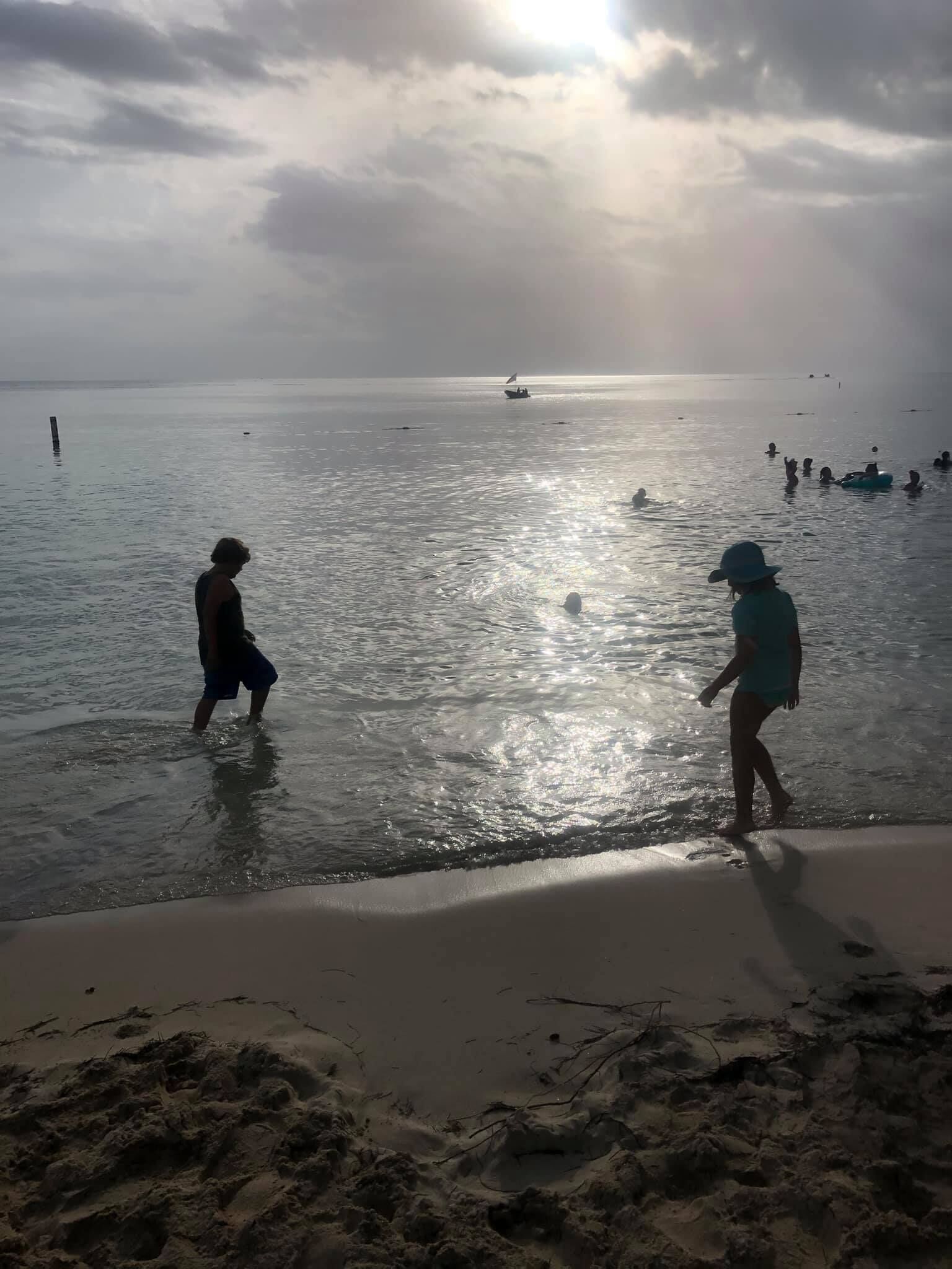A beach with people in the water and a boat in the distance.