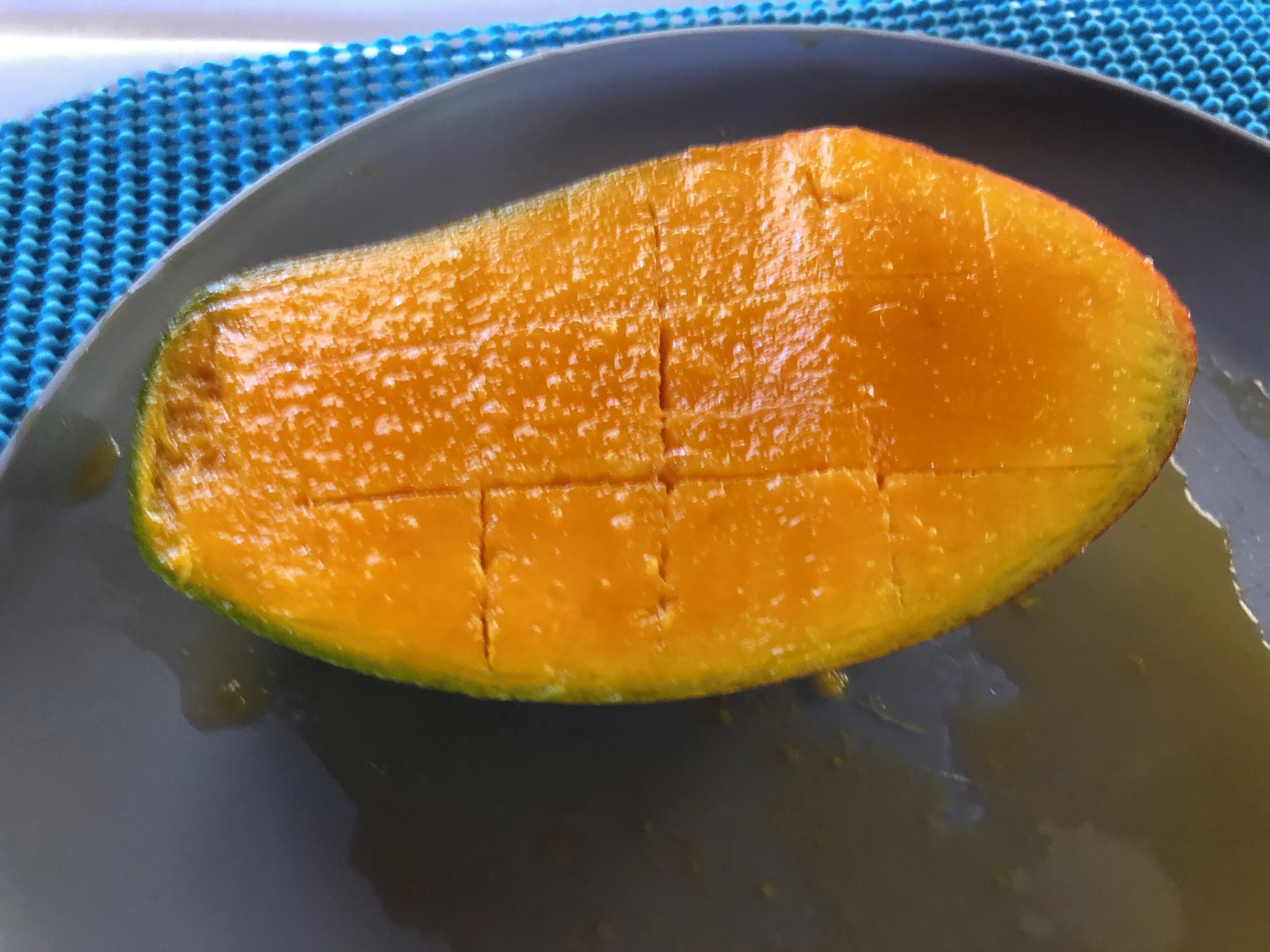 Une mangue coupée en tranches et disposée sur une assiette sombre.