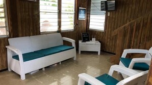 A room with a white wicker sofa and chairs, a small table with a TV, and wooden walls.
