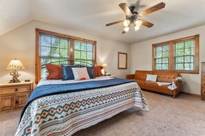 A bedroom with a large bed, a wooden headboard, a ceiling fan, and two windows with blinds.