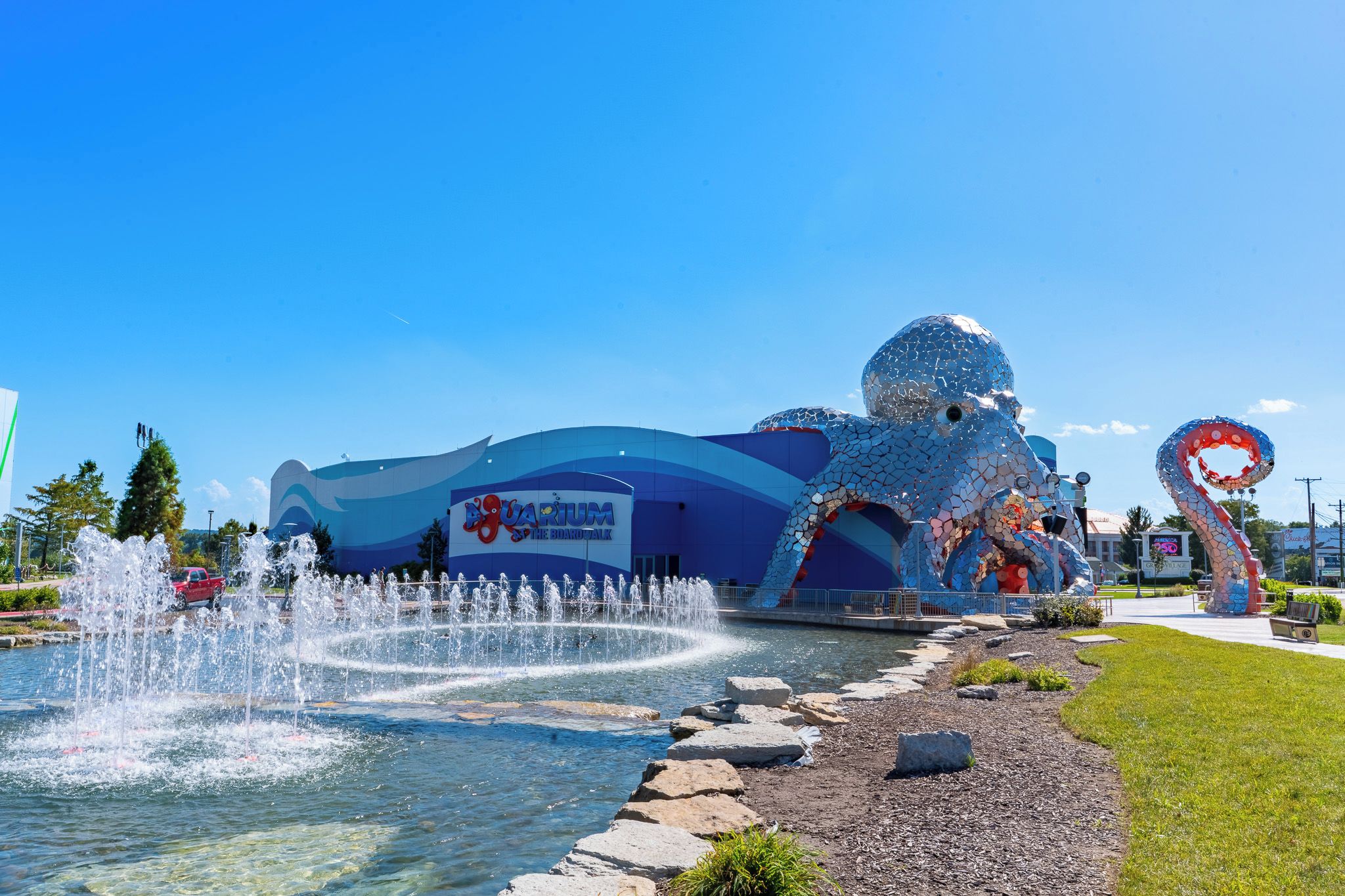 Ein Trinkbrunnen, eine große Mosaikskulptur und ein Gebäude mit einem Schild.