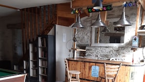 Una sala de estar acogedora con una mesa de billar, un sofá cómodo, una zona de bar con taburetes y una estantería.