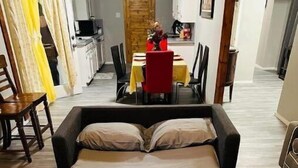 A bedroom with a bed, a dining area with a table and chairs, and a kitchen in the background. - Charming Downtown Home on 5th street (Midlothian)