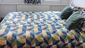 A bed with a geometric patterned bedspread, two pillows, and a window with blinds. - Room-cosy Room In Antwerpen (Mortsel)