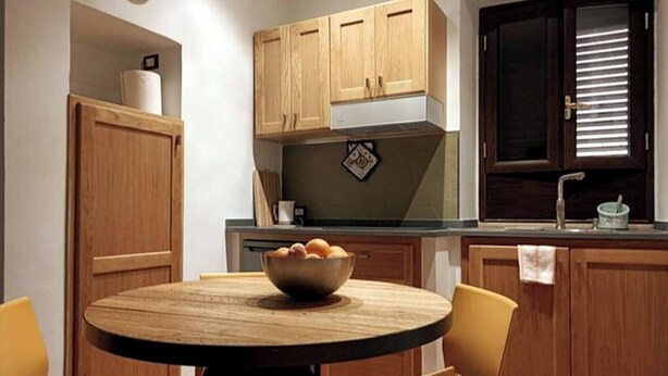 A kitchen with wooden cabinets, a round table with chairs, and a bowl of fruit on the table. - Holiday Home Sofia Palermo (Palermo)