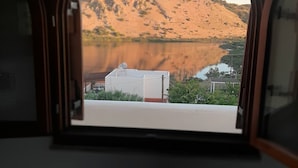 En utsikt från ett fönster över ett bergigt landskap med en sjö eller ett annat vattendrag och en byggnad i förgrunden.