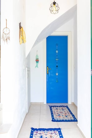 Un pasillo con una puerta azul, una pared blanca y una alfombra estampada.