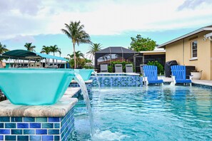 A swimming pool with blue-tiled edges, a covered area with chairs, and palm trees in the background. - Cape Coral Paradise, Waterfront, Patio, Pool, Spa, Dock, 2 blocks to open water (Cape Coral)