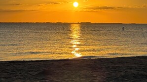 Un coucher de soleil sur une mer calme, avec une côte lointaine à l’horizon.