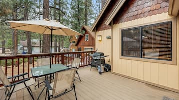 A wooden deck with outdoor furniture, a grill, and a large window.