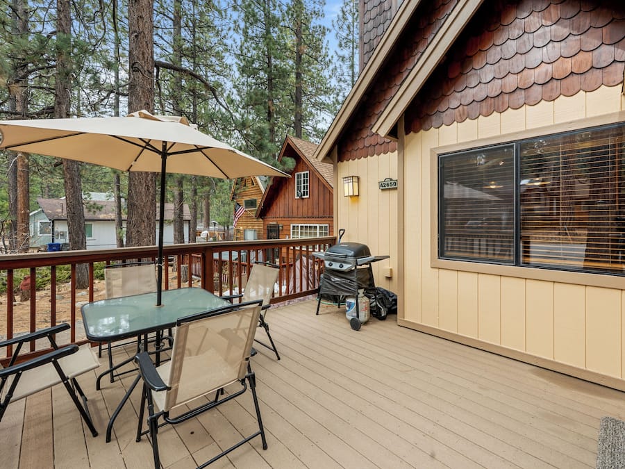 A wooden deck with outdoor furniture, a grill, and a large window.