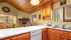 A kitchen with wooden cabinets, a dishwasher, and a stone fireplace. - Moonridge Heaven (Big Bear Lake)