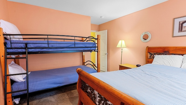 A room with bunk beds, a wooden bed, a nightstand, a lamp, and a framed picture on the wall. - Moonridge Heaven (Big Bear Lake)