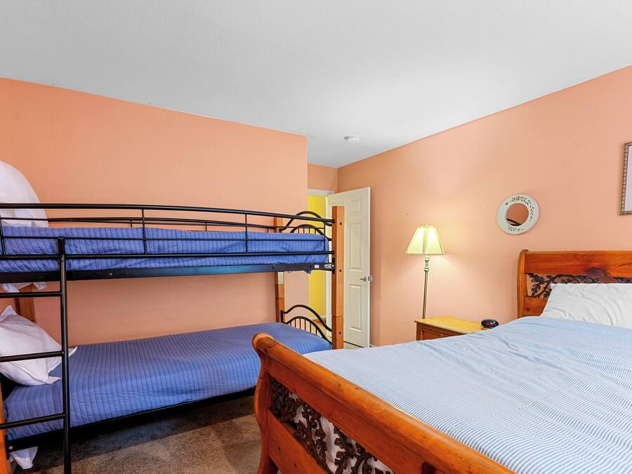 Quarto com beliches, uma cama de madeira, uma mesa de cabeceira, um abajur e um quadro na parede.