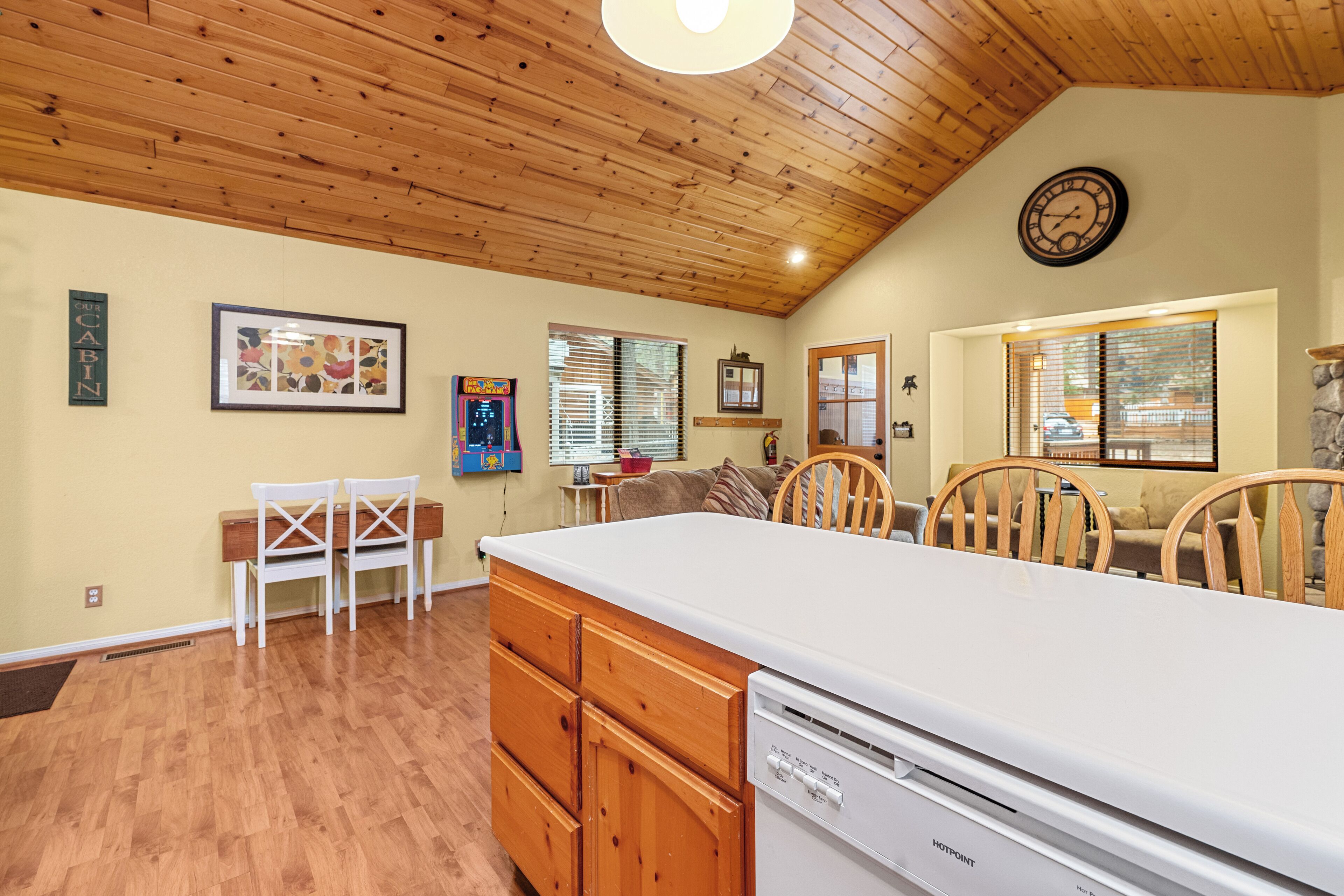 A kitchen with wooden cabinets, a white countertop, and a dishwasher. There is a dining area with chairs and a table.
