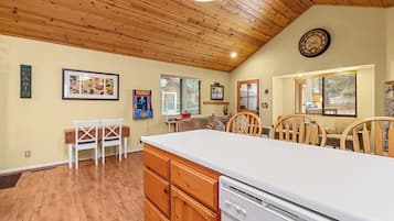 A kitchen with wooden cabinets, a white countertop, and a dishwasher. There is a dining area with chairs and a table.