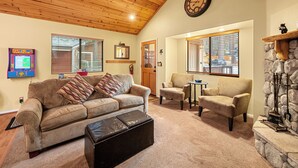 A cozy living room with a wooden ceiling, a stone fireplace, a sofa, a coffee table, and a fireplace mantel. - Moonridge Heaven (Big Bear Lake)