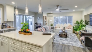 A modern kitchen with white cabinets, a central island, pendant lights, and a dining area with a coffee machine. - Newly Built Maple Valley Vacation Rental w/ Patio! (Maple Valley)