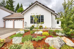 A single-story house with a garage, a well-maintained garden with various plants and rocks, and a clear view of the sky.