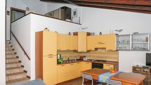 Une cuisine de taille réduite avec des meubles de couleur jaune, une table à manger avec des chaises, un canapé et un escalier.