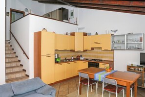 A compact kitchen with yellow cabinets, a dining table with chairs, a sofa, and a staircase.
