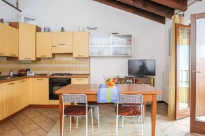 Una cocina con armarios amarillos, una mesa de madera, dos sillas, un televisor y una ventana con cortinas.