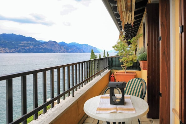 A balcony with a view of a lake and mountains, a table with a chair, and potted plants.