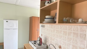 A compact kitchen with a white refrigerator, a gas stove, a sink with a pink basin, and wooden shelves above holding dishes and glasses. - Sedef Pansiyon Apart Otel Sarkoy (Sarkoy)