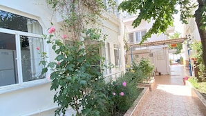 A narrow, tiled pathway leading to a building with a white facade, surrounded by greenery and a small garden area. - Sedef Pansiyon Apart Otel Sarkoy (Sarkoy)