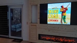 Un salon moderne avec un téléviseur à écran plat fixé sur un mur en bois, une porte-fenêtre coulissante donnant sur un balcon et une cheminée située sous le téléviseur.
