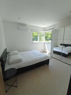 Ein modernes Schlafzimmer mit Bett, Stuhl, Fenster und Spiegel.