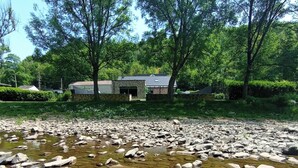 Une propriété située au bord de la rivière, avec un bâtiment en pierre, entourée d’une végétation luxuriante et d’arbres.