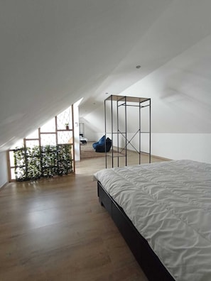 A modern, spacious bedroom with a sloped ceiling, a large bed, a seating area with a chair, and a view of the outdoors.